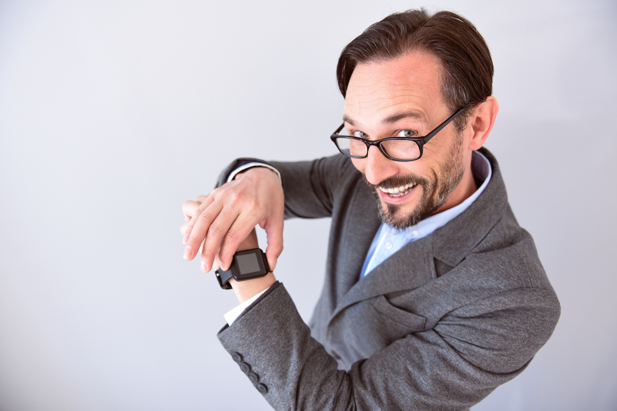 It is very useful. Confident mature man with smile on his face touching and showing a smart watch on his wrist isolated on the grey background